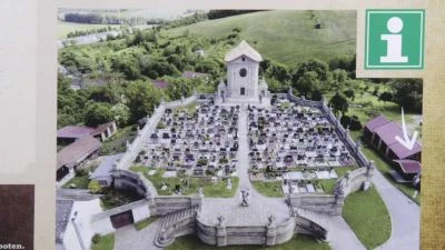 Barokní hřbitov s kostelem na kopci v krajině.