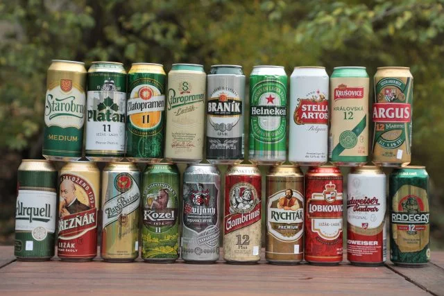Různé české pivo v plechovkách na dřevěném stole venku.