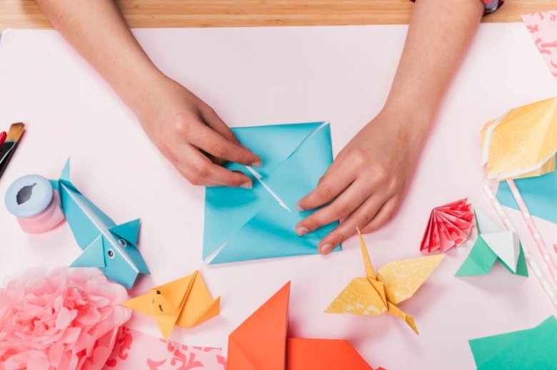 Ruční práce s papírem - skládání origami na stole.