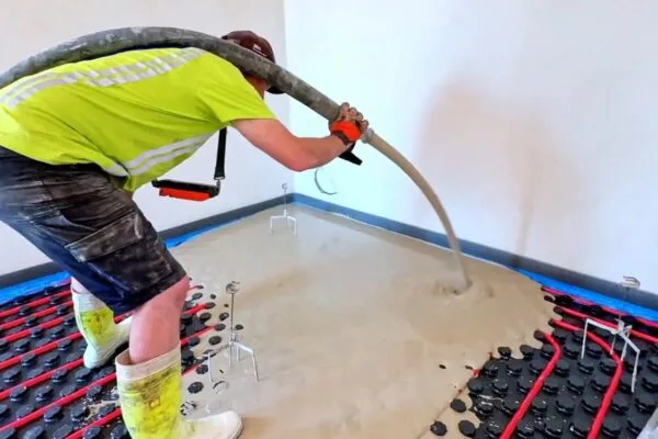 Stavebník nalévá beton na podlahu s topnými trubkami.