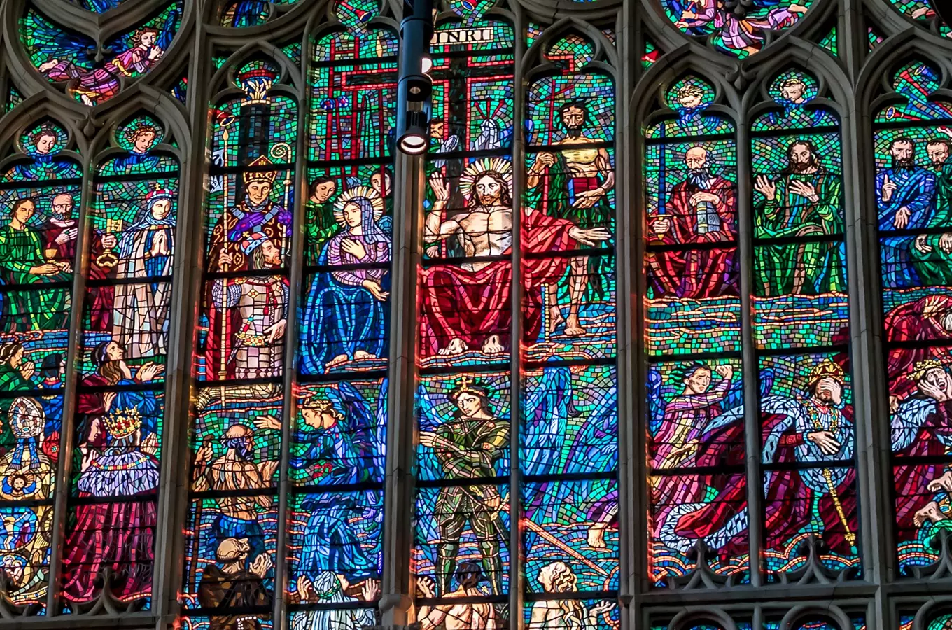 Detailní fotografie barevného vitráže s biblickými scénami v gotickém stylu.