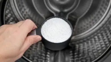 Ruka s měřičem bílého prášku v bubnu pračky pro čištění.