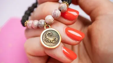 Zlatý amulet s obrázkem Skorpiona na náramku v ruce.