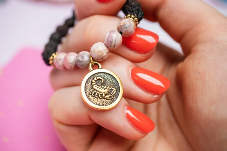 Zlatý amulet s obrázkem Skorpiona na náramku v ruce.