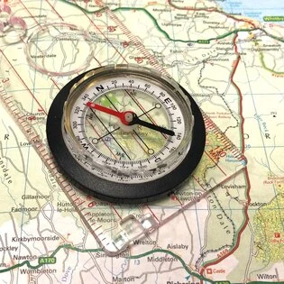 Kompas položený na turistické mapě pro orientaci v terénu.