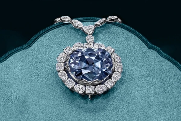 Modrý diamant v náhrdelníku s drobnými brylanty na tyrkysovém podkladu.