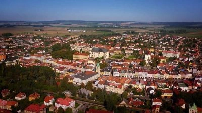 Pohled na historické město s červenými střechami a zelení.