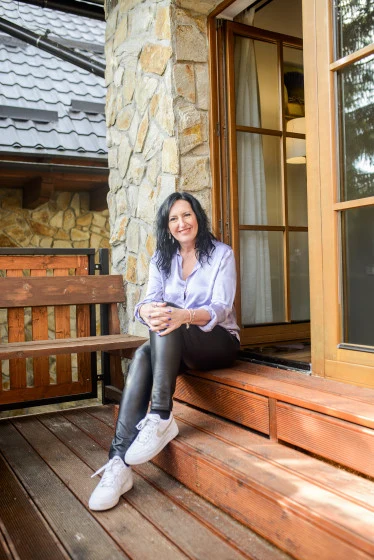 Žena sedí na schodech venku u domu s přátelským výrazem.