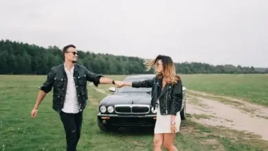 Muž a žena se drží za ruce vedle auta na louce.