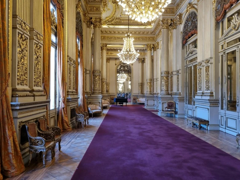 Luxusní palácová hala s fialovým kobercem a zlatými detaily.
