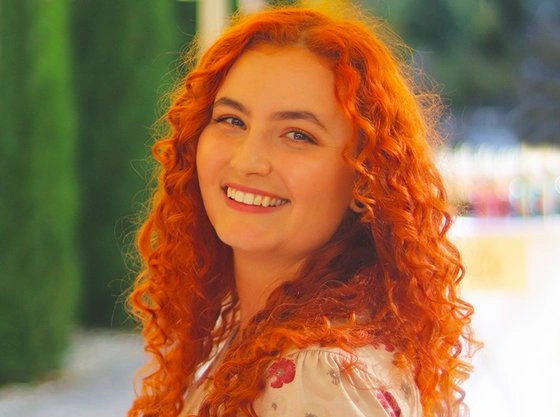 Usměvavá žena s červenými vlasy na pozadí zelené zdi.